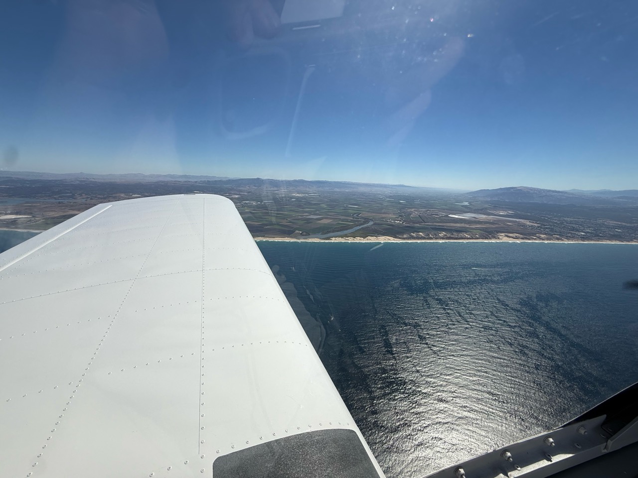 An airplane wing above the coastline and blue ocean
